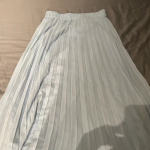 Ljusblå långkjol från Monki - Säljer en ljusblå långkjol från Monki me design och resår i midjan. Kjolen har en luftig och flowy känsla, perfekt för varmare dagar. Enkel att matcha med olika toppar för en stilren look.