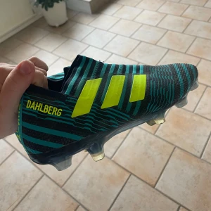 Adidas Nemeziz blå fotbollsskor - Säljer ett par Adidas Nemeziz fotbollsskor i blått och svart med neongula ränder. Skorna kommer med utbytbara dobbar (skruvdobbar), dem är helt oanvända, och utan skosnöre vilket jag föredrar. Storlek 40 (us7). Står Dahlberg på sidan, syns inte så mycket:) 