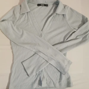 Ljusblå ribbad kofta från Bik Bok - Säljer en ljusblå ribbad kofta från Bik Bok i storlek XS. Koftan har v-ringning, krage och knappar framtill. Den är långärmad och har en slim passform som sitter snyggt på kroppen. Perfekt att slänga över en topp eller linne.