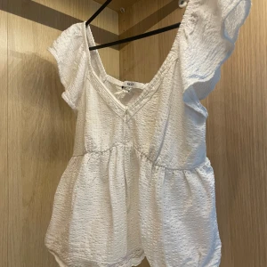 Vit blus med volangärm från Next - Supersöt vit babydoll blus från Next med korta volangärmar och v-ringning. Toppen har en luftig, lätt struktur med diskret textur i tyget. Passar S och M. I princip inte använd. 