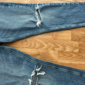 Blå ripped jeans från Zara - Snygga blå jeans från Zara med slitna hål över knäna för en trendig, avslappnad look. Klassisk femficksmodell med normal passform och hög midja. Jeansen är i denim och har en lätt tvättad finish som ger en cool vibe.