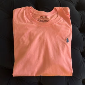 Rosa t-shirt från Polo Ralph Lauren - Snygg rosa t-shirt från Polo Ralph Lauren med klassisk blå logga broderad på bröstet. Är i riktigt bra skick ( knappt använt) 9/10. Storlek -M. Färgen ser annorlundare ut på andra bilden pågrund av ljuset. Funderingar osv, Dma🤙