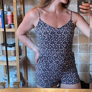 Jumpsuit - Söt jumpsuit från Divided H&M i svart med små rosa, vita och blå blommor. De har en loose passform och är perfekta för sommaren. Materialet är mjuk bomull och shortsen har resår i midjan för extra komfort.