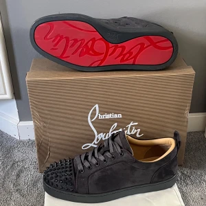 Christian Louboutin skor  - Mörk gråa sneakers i mocka från Christian Louboutin med ikonisk röd sula och svarta nitar på tån. Skorna har rund tå, snörning och en lyxig känsla med beige innersida. Perfekta för dig som vill sticka ut med din stil. Skorna är använda 2 gånger och allt ingår + extra spikar. Skriv vid frågor, pris är ej hugget i sten!! 