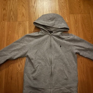 Grå hoodie från Polo Ralph Lauren - Säljer en klassisk grå hoodie från Polo Ralph Lauren.Pågrund av att den har blivit för liten. Skick 8/10 inga fläckar. Hör av er vid frågor. Pytte litet hål i ryggen som inte syns vid användning 