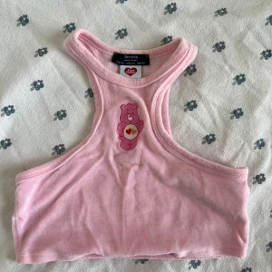 Rosa Care Bears croppad linnetopp XS - Supersöt ljusrosa croppad linnetopp från Bershka x Care Bears. Toppen har broderad Care Bears-nalle framtill och är i mjuk frottéliknande bomullsblandning. Perfekt för dig som gillar gulliga detaljer och vill sticka ut med en unik topp. Jag säljer även en lilla. 