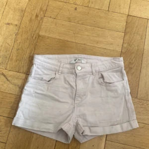 Ljusbeige shorts från H&M, strl 152 - Snygga ljusbeige shorts från H&M med klassisk femficksmodell, uppvikta benslut och bälteshällor. Perfekta för varma dagar och enkla att matcha med allt. Gjorda i mjuk bomull för skön känsla hela dagen.
