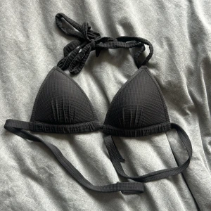 Svart ribbad trekantsbikini - Snygg svart trekantsbikini med ribbad struktur och knytband i nacken och ryggen. Klassisk och stilren modell som passar perfekt till stranden eller poolen. Materialet känns mjukt och följsamt mot huden.