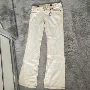 Vita bootcut jeans med röda detaljer - Snygga vit/beiga jeans med bootcut-modell Byxorna har röda sömdetaljer och en liten metallring framtill. Perfekta i längden för mig som är 170 men tyvärr lite små i midjan. Finns lite små fläckar som nog inte syns men säkert försvinner i tvätten.