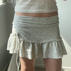 Blommig volangkjol från Gina Tricot XS - Supersöt  kjol från Gina Tricot i ljusgrönt med små blommor och volangkant. Kjolen har snörning på sidan som är skysterbar. Man kan även om man vill använda kjolen som en topp 