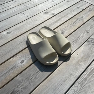 Adidas Yeezy Slide i beige - Säljer ett par Adidas Yeezy Slide i beige. De har en chunky, vågformad sula och är tillverkade i syntetmaterial. Slidesen har öppen tå och minimalistisk design med Adidas-logga på innersulan. Perfekta för sommaren och chill dagar. Ej äkta 