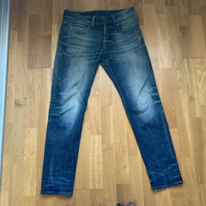 Blå G-Star raw  jeans med slitningar W29 L32 - Snygga blå jeans med slitna detaljer och ljusare partier på lår och knän. Klassisk femficksmodell med raka ben och normal passform. Jeansen har en cool tvättad look och är tillverkade i robust denim.