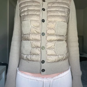 Moncler cardigan jacka  - Snygg beige quiltad cardigan jacka  från Moncler med stickade ärmar och två stickade fickor framtill. Fint skick, några trådar som sticker ut på ärmen men går enkelt att få tillbaka med en virknål. I övrigt fint skick, inga hål eller liknande. Storlek L men passar även mindre