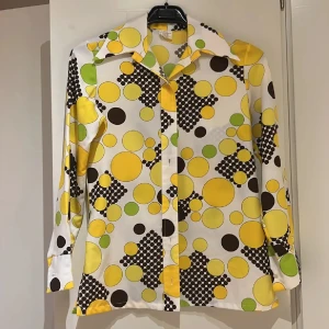 Äkta 70-tals skjorta - ÄKTA 70-TALS SKJORTA! Snygg retroinspirerad skjorta med stora och små prickar i gult, brunt och grönt på vit botten. Skjortan har bred krage, långa ärmar och knäppning framtill. Perfekt för dig som gillar färg och mönster med 70-talsvibbar. (Inköpt dyr ny till second hand butik) M i storlek men känns som en S!