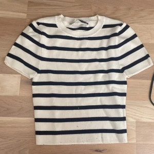 Randig stickad topp i marin stil - Snygg stickad topp med kort ärm i vit och marinblå randigt mönster. Klassisk rund halsringning och rak passform. Perfekt för dig som gillar en stilren och tidlös look med lite fransk vibe.