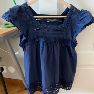 Mörkblå blus med spets från Big Star - Supersöt mörkblå blus från Big Star med broderade spetsdetaljer vid halsringning, ärmar och nederkant. Blusen har en luftig passform, korta volangärmar och fyrkantig ringning. Perfekt för dig som gillar romantiska och boho-vibbar. Storlek M men liten i storlek så passar nog xs/s.