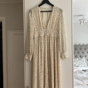 Lång blommig klänning från Adoore - Superfin långklänning från Adoore i ljusbeige med små gula blommor. Djup v-ringning, knappar framtill och långa ärmar med lätt puff. Klänningen har ett flowy fall och markerad midja, perfekt för sommarens alla tillfällen. Särskild till midsommar!😍Klänningen är enbart använd 1 gång, i inomhus miljö så klänningen är i nyskick. Nypris är 1500kr säljer för 700kr. 
