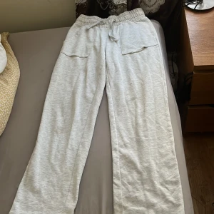 Ljusgrå mjukisbyxor med stora fickor - Ljusgrå mjukisbyxor i bomull med bred resår och snörning i midjan. Byxorna har två stora, fyrkantiga fickor framtill och raka ben. Perfekta för chill dagar eller när du vill vara extra bekväm.