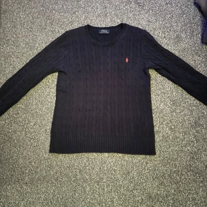 Mörkblå stickad tröja Ralph Lauren - Kabelstickad mörkblå tröja från Polo Ralph Lauren med klassisk rund halsringning och röd broderad logga på bröstet.