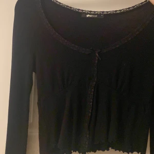 Svart kofta med spets från Gina Tricot - Supersöt svart kofta från Gina Tricot med spetsdetaljer längs halsringningen och knäppning framtill. 