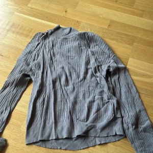 Grå ribbad polotröja - Säljer en grå ribbad polotröja med lång ärm och hög krage. Tröjan har en snygg, smal passform och är perfekt för lager-på-lager. Materialet känns mjukt och stretchigt, vilket gör den riktigt skön att ha på sig.