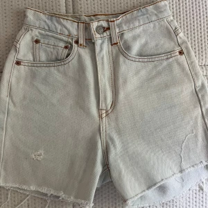 jeansshorts  - Snygga ljusa jeansshorts från Levi's I bra skick. Shortsen har råa, fransiga benslut och slitning framtill för en cool vibe. 31 cm midja. Perfekta för sommaren!