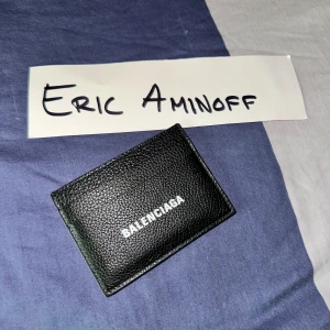 Oanvänd Svart Balenciaga korthållare - Minimalistisk svart plånbok från Balenciaga i äkta skinn med vit logga framtill. Plånboken har flera kortfack och stilren design med grynig textur. Perfekt för dig som vill ha en exklusiv och lyxig accessoar! Helt oanvänd men tyvärr har jag inte kvar lådan någonstans. Hittar jag den så får du självklart med en låda till köpet :)