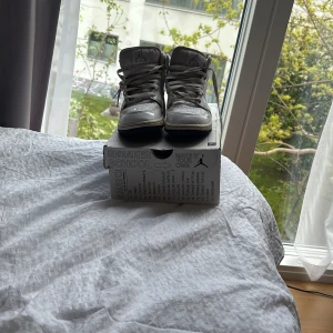 Nike Air Jordan 1 Mid SS White/Black - Säljer ett par Nike Air Jordan 1 Mid SS i vitt och svart. Skorna har högt skaft, svart sula och coola handskrivna detaljer på ovandelen. Klassisk Jordan-logga på sidan och snörning framtill. Perfekta för dig som gillar streetstyle.