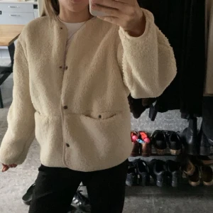 Beige teddyjacka med knappar - Säljer denna populära teddyjackan med rund halsringning och knäppning framtill. Jackan har två fickor och en avslappnad passform, perfekt för att hålla värmen under kyliga dagar. 💓