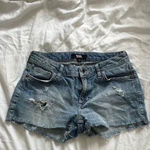 Blå jeansshorts Low waist - Säljer ett par blå jeansshorts från Denim Co. med råa kanter och slitna detaljer framtill. Klassisk femficksmodell med knapp och dragkedja. Perfekta för en avslappnad stil. Storlek 158 men passar också xs