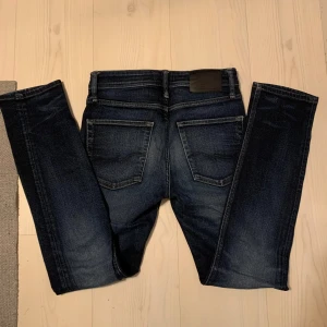 Mörkblå slim fit jeans - Säljer ett par mörkblå slim fit jeans med klassisk femficksdesign och snygga slitningar. Modellen heter 'Tim' och har raka ben. Perfekta för dig som gillar en smalare passform. Storlek W28/L32.