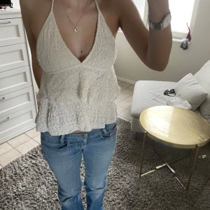 Vit halterneck linnetopp - Säljer en söt vit halterneck topp med volangdetaljer och struktur i tyget. Toppen är ärmlös och knyts i nacken, vilket ger en öppen rygg. Perfekt för varma dagar och somriga outfits.☀️🌺Storlek L men väldigt liten i storlek då den passar mig som har S-M i storlek 