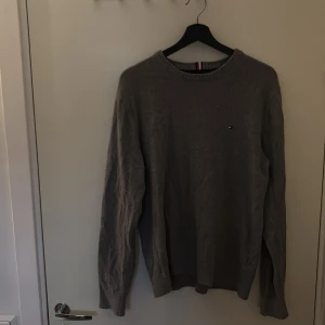 Grå tröja från Tommy Hilfiger - Säljer en stilren grå tröja från Tommy Hilfiger i pima cotton blend med cashmere. Klassisk rund halsringning och diskret logga på bröstet. Perfekt för dig som gillar enkel och snygg stil.