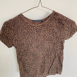 Leopardmönstrad croppad t-shirt från Brandy Melville - Säljer en brun croppad t-shirt från Brandy Melville med leopardmönster. T-shirten har rund halsringning och korta ärmar. 