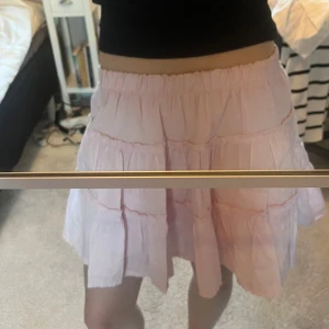 Ljusrosa volangkjol - Söt ljusrosa kjol med flera volanger och resår i midjan. Kjolen är kort och har en luftig känsla, perfekt för varmare dagar. Passar dig som gillar en feminin och lekfull stil.