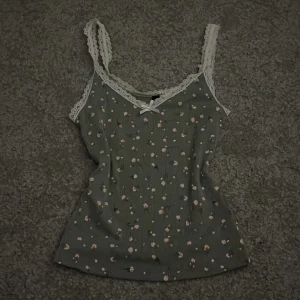Blommigt linne med spets från H&M - Säljer detta  blommiga och gröna linnet ifrån Devided/H&M med jättefina spetsdetaljer på banden. Dessutom en liten rosett vid bysten. Köpt för längesedan men har aldrig använts💗