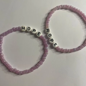 Ljuslila pärlarmband med HOPE-bokstäver - Två armband med ljuslila pärlor och vita bokstavspärlor som bildar ordet HOPE. Perfekt accessoar för att sprida positivitet och stil.