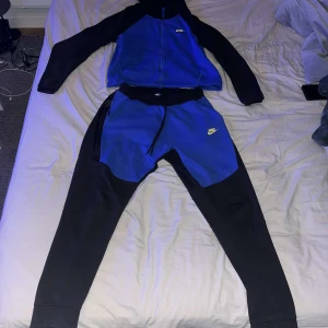 Blå och svart og tracksuit från Nike - Säljer en og nike tech tracksukt från Nike i blått och svart med dragkedja och huva. två fickor framtill. Perfekt för dig som gillar sportig stil och vill ha något bekvämt och trendigt. Den e knappt använd köpt för länge sen. Kan gå ner i pris vid snabb affär!!