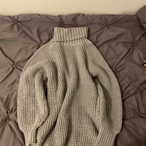 Grå stickad polotröja - Mysig grå stickad polotröja med grovstickat mönster och hög polokrage. Perfekt för kyliga dagar och enkel att matcha med olika outfits. Långa ärmar och ribbade muddar för extra komfort.