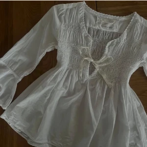 Odd Molly blus  - vit blus från Odd molly med smockad överdel, knyt framtill och volangdetaljer. Perfekt för vår och sommar!