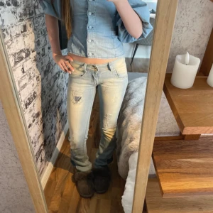 Ljusblå slitna jeans från MET - Säljer ett par ljusblå jeans från MET med slitningar och hål på benen. Jeansen har låg midja, utsvängda ben och dubbla knappar i midjan. Klassisk femficksmodell och snygg tvätt med slitna detaljer. De är klippta till bootcut se näst sista bilden
