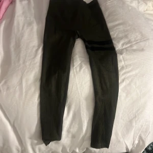 Mörkgröna träningstights från Stronger - Snygga mörkgröna tights från Stronger med hög midja och ribbade detaljer. Perfekta för träning och har en diskret logga i midjan. Materialet är stretchigt och bekvämt.