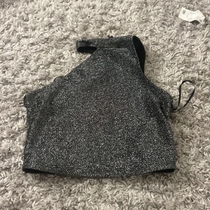 Glittrig oneshoulder topp från SHEIN - Säljer en glittrig silverfärgad oneshoulder topp från SHEIN. Toppen har en croppad passform och är perfekt för dig som vill sticka ut. Materialet är syntet och toppen har en snygg asymmetrisk design.