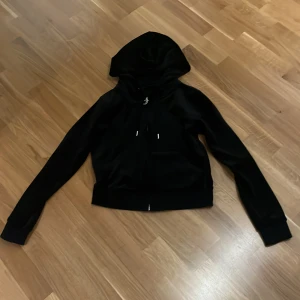 Svart velour hoodie från Juicy Couture - Säljer en svart hoodie från Juicy Couture i mjuk velour. Jackan har huva, dragkedja med J-hänge och långa ärmar. Inte använd så många gånger.