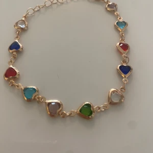 Armband med hjärtformade färgade stenar - Superfint armband med små hjärtan i olika färger, infattade i guldfärgad metall. Hjärtana är i blått, rött, grönt, turkost, vitt och lila. Perfekt accessoar för att addera färg till din look. Armbandet e nytt och knappt använt🥰 priset går att diskutera!💞