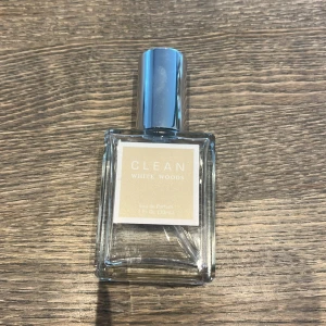CLEAN White Woods Eau de Parfum - En elegant parfym från CLEAN med doften White Woods. Flaskan är rektangulär i genomskinligt glas med en stilren, silverfärgad kork och en ljus etikett framtill. Perfekt för dig som gillar fräscha och träiga doftnoter.