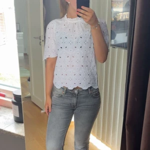 Vit blommig blus  - Säljer en söt vit blus med blommigt broderi. Blusen har korta ärmar och en hög halsringning. Jätte söt blus perfekt till sommaren!!