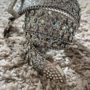 Glittrigt silverbälte med strassdetaljer - Säljer ett riktigt snyggt bälte i silver med massor av glittrande strass och nitar. Bältet har en bred spänne täckt av stenar och hela bältet är dekorerat med glittriga detaljer som verkligen sticker ut.
