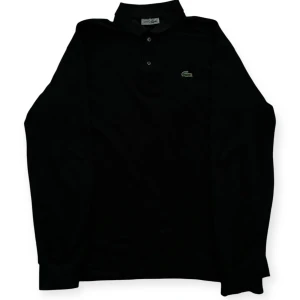 Svart tröja från Lacoste - Klassisk svart pikétröja från Lacoste med krage och knappar framtill. Tröjan är långärmad. Perfekt för sommaren. 