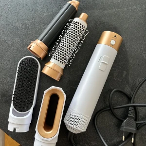 Multifunktionell Hot Air Styler med flera munstycken - Säljer en vit och guldig hot air styler med flera utbytbara munstycken, inklusive rundborste, locktillbehör och fönmunstycke. Kommer med ett till munstycke som inte syns på bilden. Perfekt för att styla håret på olika sätt med ett och samma verktyg. 220-240V, 1000W.